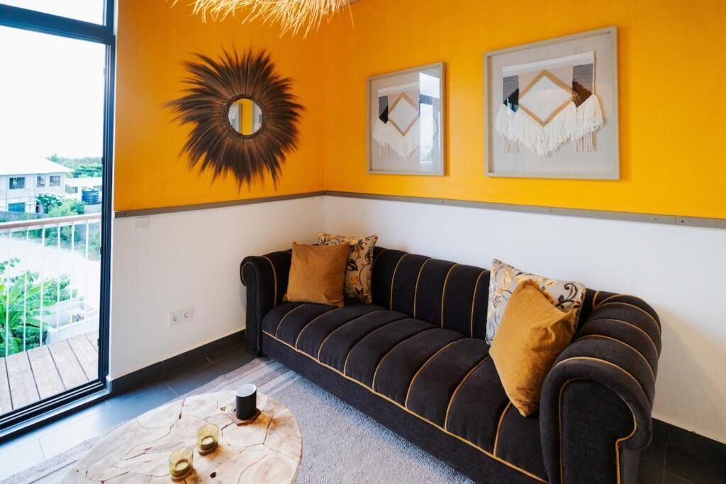 A room with a dark sofa, two pillows, a round mirror, and two framed artworks on the wall.