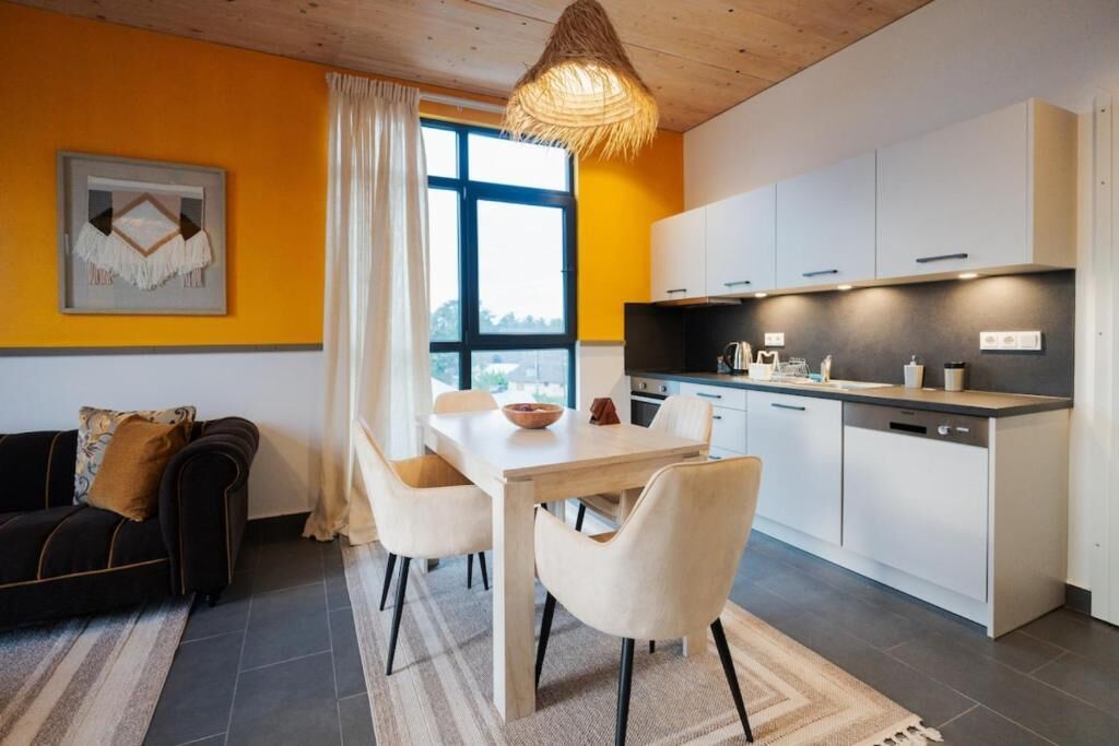 A modern kitchen with white cabinets, a dining table with chairs, and a large window with curtains.