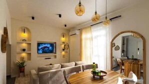 A modern living room with a sofa, a wooden dining table, and a television. - Nafsi Nomad (Paje)