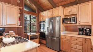 Una cocina con armarios de madera, electrodomésticos de acero inoxidable, una estufa a gas y una ventana con persianas.