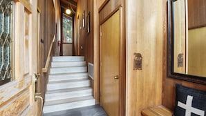 Una escalera de madera que conduce a una habitación con una puerta de madera, un banco y un espejo fijado a la pared.