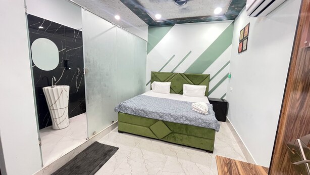 Une chambre à coucher moderne avec un lit recouvert d’un tissu vert, une couvre-lit blanche et grise à motifs, et un sol carrelé en marbre.