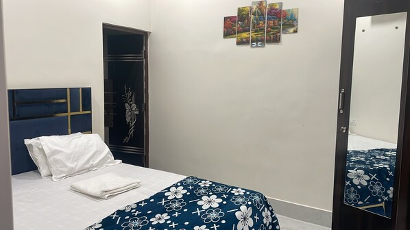 A bedroom with a bed, a wardrobe, a mirror, and a wall with artwork.