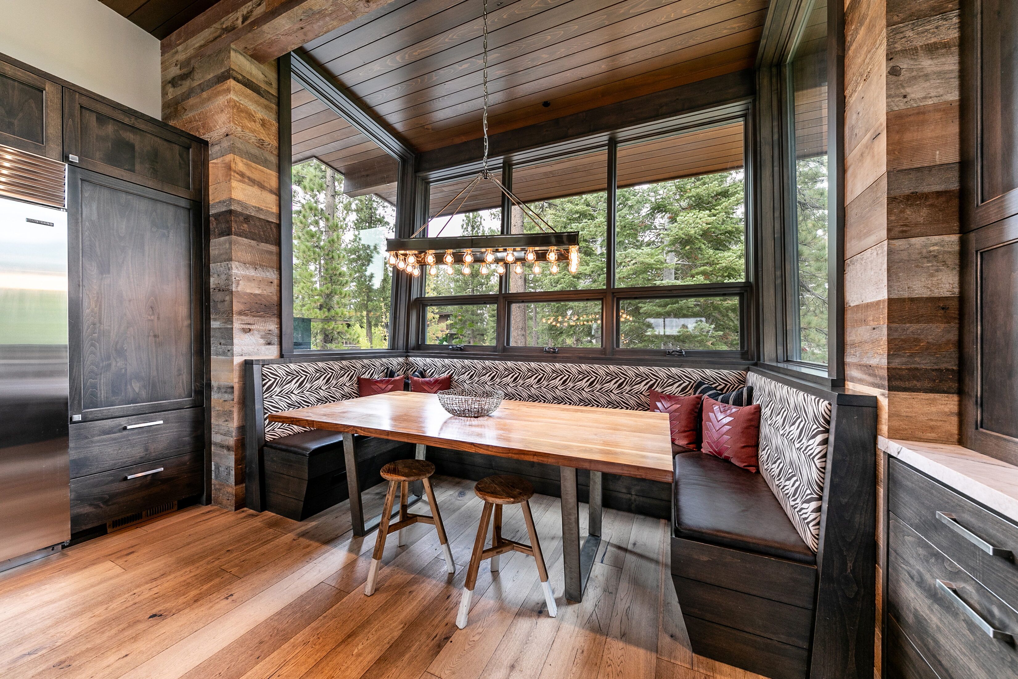 Una cocina moderna con un banco y taburetes de madera, ventanas amplias y una lámpara colgante.