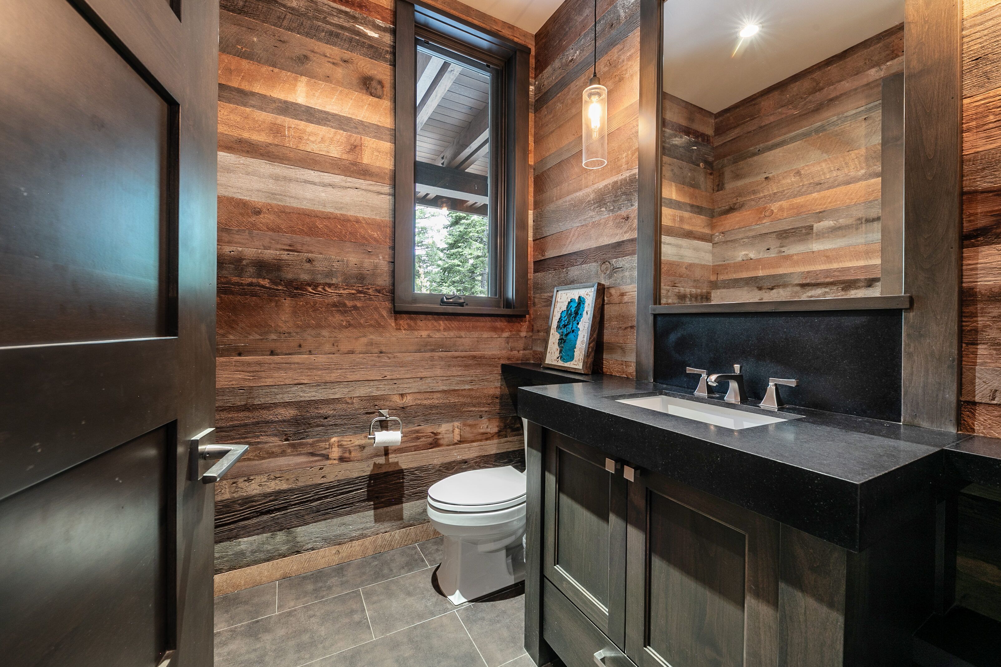 A modern bathroom with wooden panel walls, a black countertop, and a white toilet.