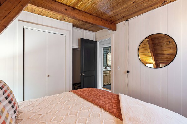 Un dormitorio con una cama, un espejo redondo y una puerta que da a una cocina.