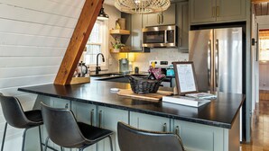 Una cocina con una isla central, taburetes de bar, un refrigerador de acero inoxidable y una lámpara colgante.