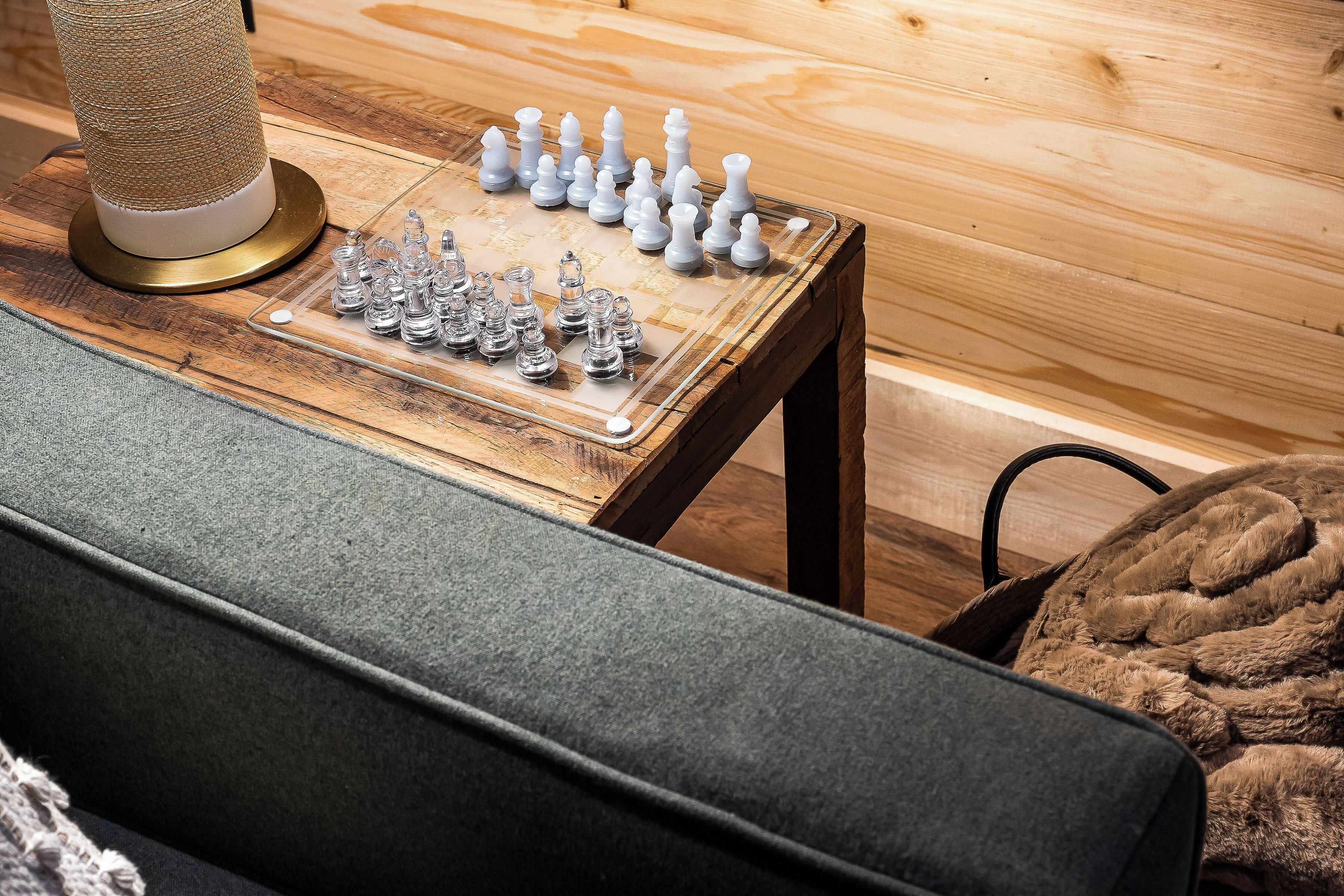 A chessboard on a wooden table with a cat tree beside it.