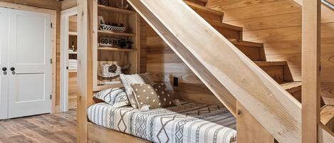 A wooden staircase leading to a loft bedroom with a bed and built-in shelves.