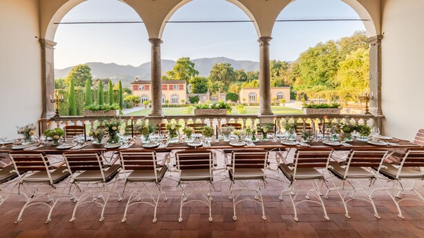 A dining area with a view of a landscaped garden and mountains. - Villa Antica in Lucca (Capannori)