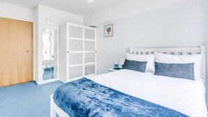 Une chambre à coucher comprenant un lit, une table de chevet, une commode, une armoire et une porte.