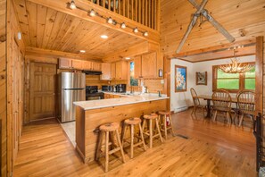 A wooden cabin interior with a kitchen, dining area, and bar stools. - 4 BR Cabin near Banner Elk/Beech Mtn. Hot Tub, Fire Pit & Yard (Banner Elk)