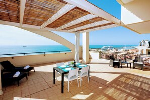 Een terras met een eettafel, lounge stoelen en uitzicht op zee en jachten.
