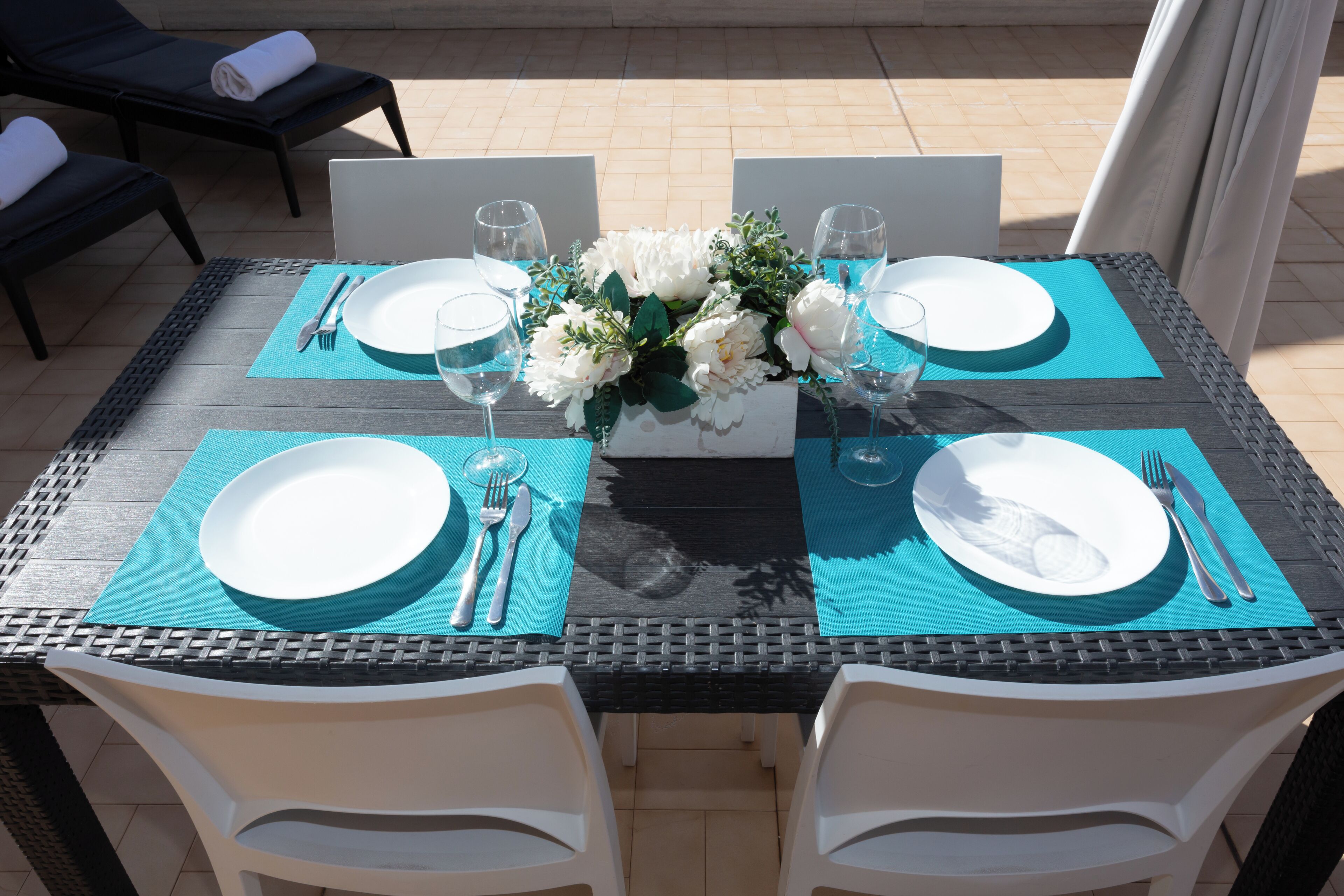Mesa de comedor lista para cuatro personas, con sillas blancas, un centro de mesa floral y un camino de mesa azul.