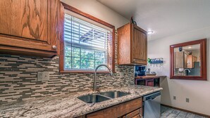 A kitchen with wooden cabinets, a granite countertop, a window with blinds, and a built-in dishwasher. - Our Comfy Cabin | Cozy Retreat w/ Foosball, Wildlife Views & Family Fun (Ruidoso)