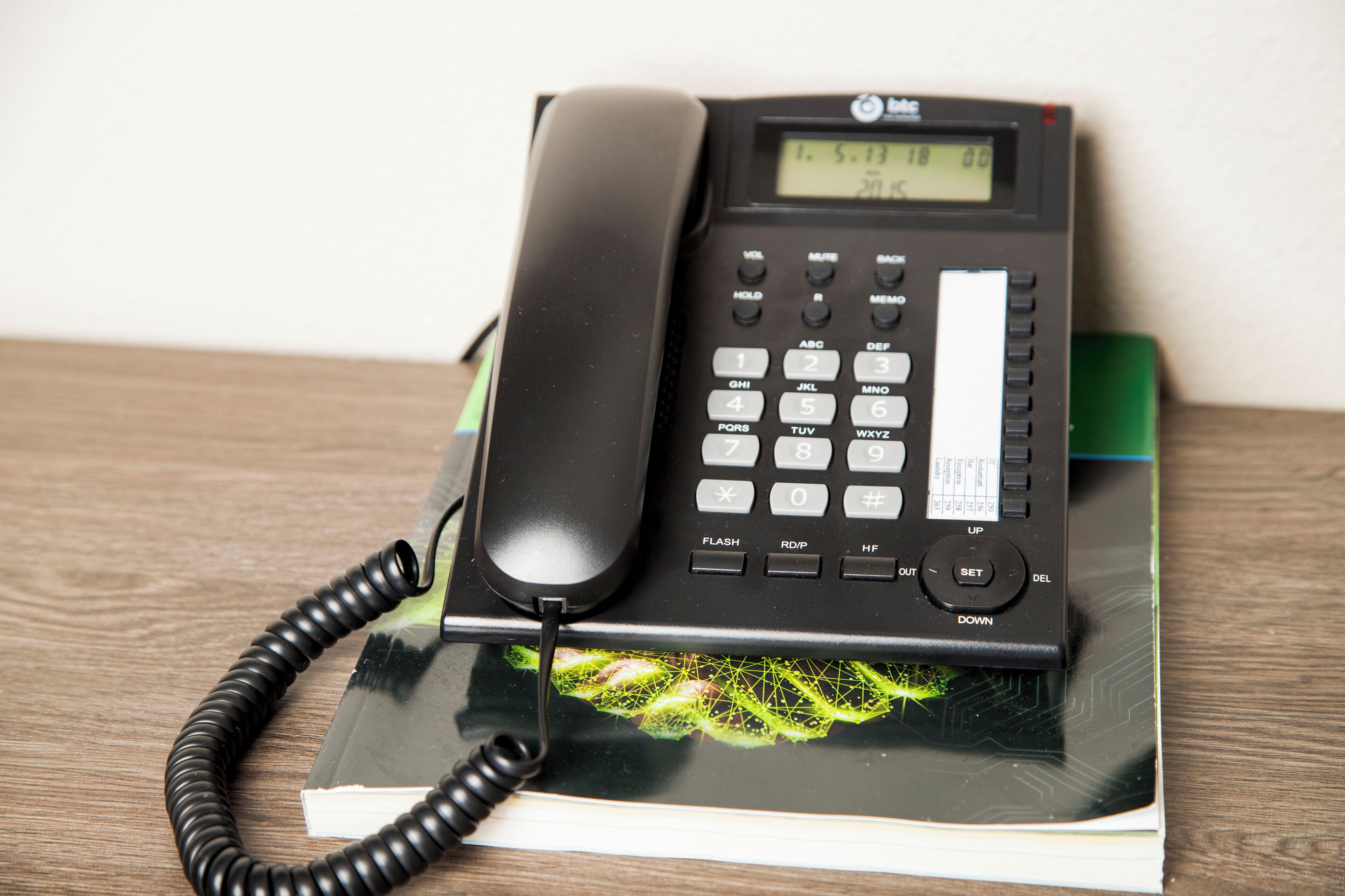 A black telephone with a coiled cord on a book with a green cover.