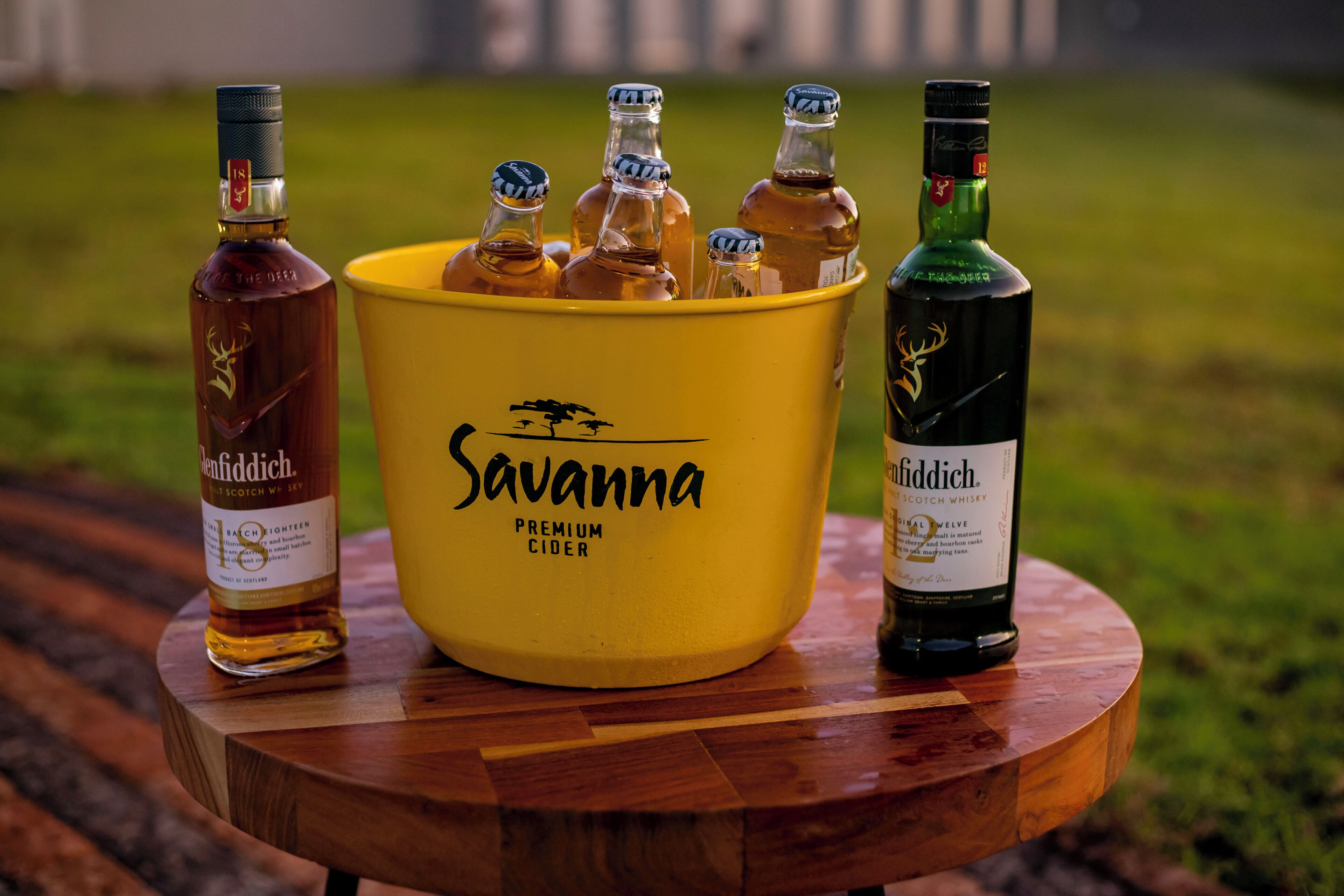 Egy fa asztal, rajta egy sárga színű, „Savanna Premium Cider” felirattal ellátott vödör, amelyben több üveg almalé és egy üveg whisky található.