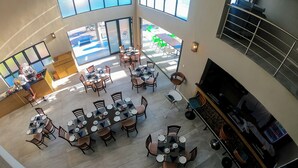 A spacious indoor area with multiple tables and chairs, a kitchen area, and a seating area with a view of the street. - Two Rivers Hotel (Kasane)