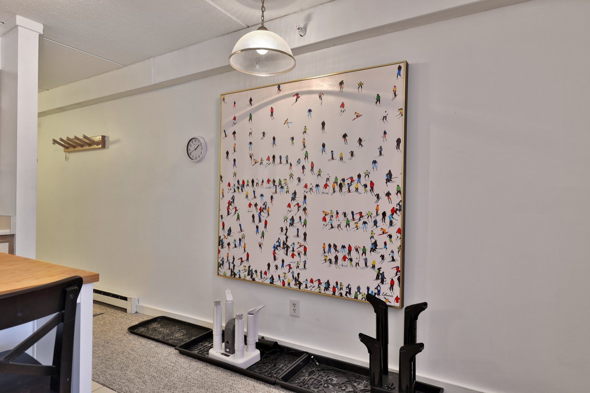 A room with a large wall mural depicting skiers, a wooden table, a chair, a clock, and a radiator.