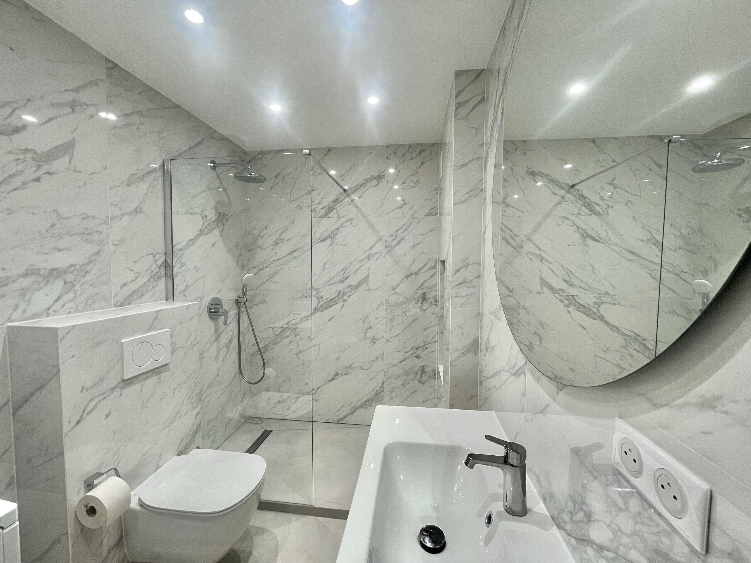 Een moderne badkamer met een marmeren wand, een douche met glazen wanden, een witte wastafel en een toilet.