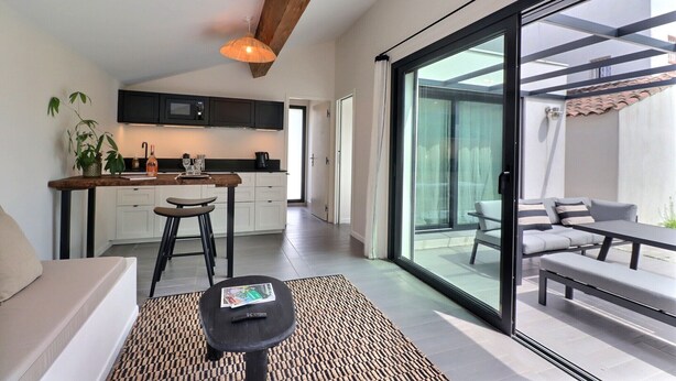 A modern kitchen with a dining area, large sliding glass doors to a patio, and a sofa with a small table. - La Cabane du Cap (Aix-en-Provence)