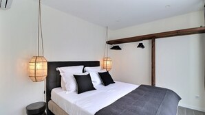 A modern bedroom with a large bed, two bedside lamps, and a wooden ceiling beam. - La Cabane du Cap (Aix-en-Provence)