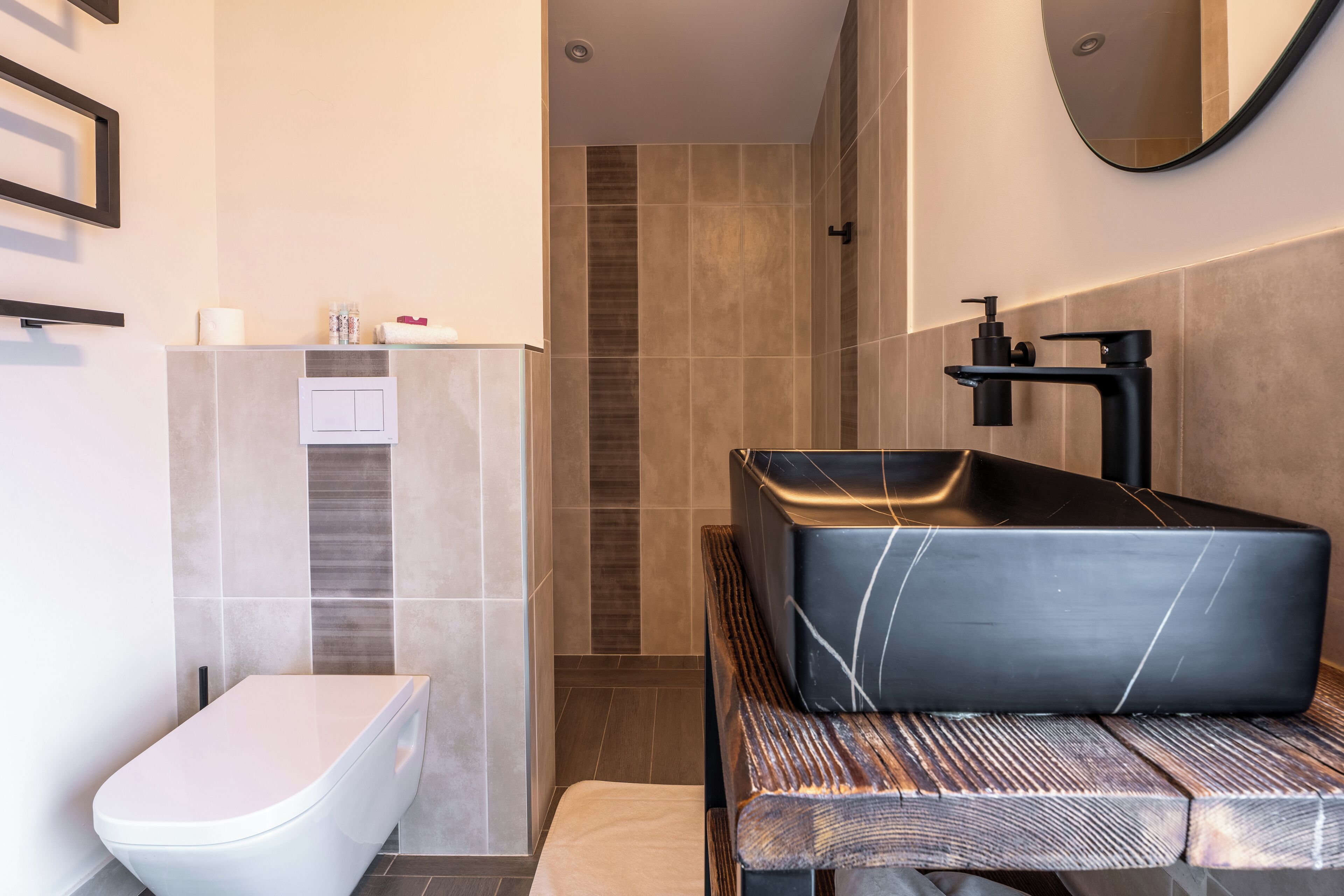 Een moderne badkamer met een wit toilet, een zwart wastafelmeubel met een marmeren kom en een houten bankje.