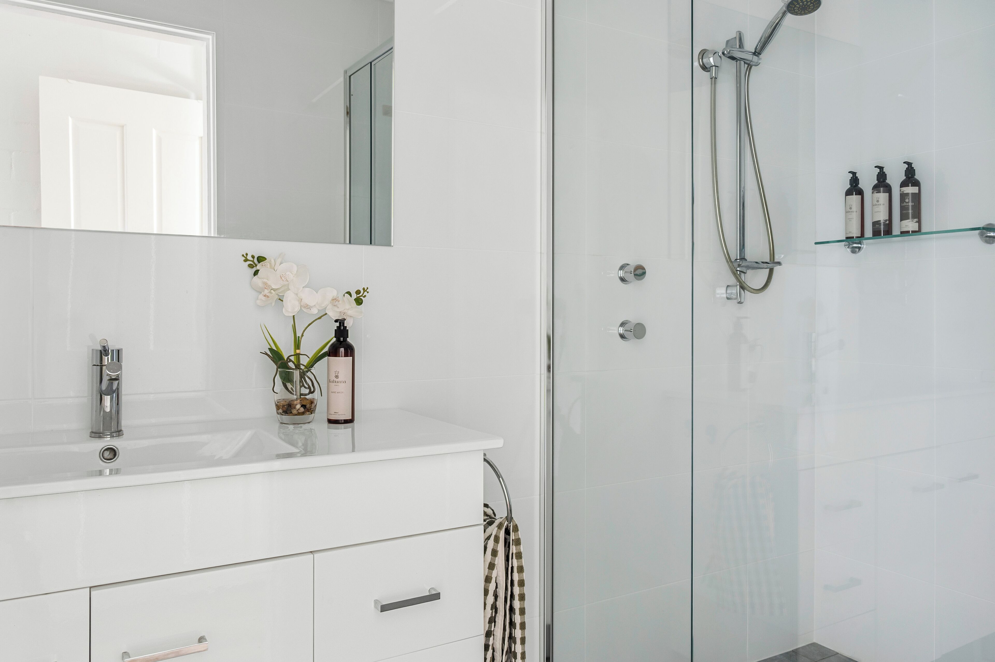 Un bagno moderno con un mobile lavabo bianco, uno sportello doccia in vetro e uno specchio sopra il lavandino.