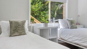 Een slaapkamer met twee bedden, wit beddengoed en een raam met uitzicht op groen.