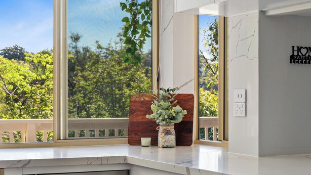 Een keuken met een groot raam, een houten snijplank, een vaas met bloemen en een bordje aan de muur.