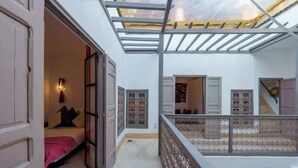 A room with a bed, a small table, and a window with decorative tiles. - Exclusive charming riad in the heart of the medina

10 mn from Jemaa el fna  (Marrakech)