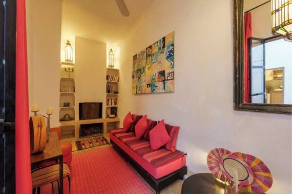 A cozy living room with a red sofa, bookshelves, a fireplace, and a colorful abstract painting. - Exclusive charming riad in the heart of the medina
10 mn from Jemaa el fna (Marrakech)