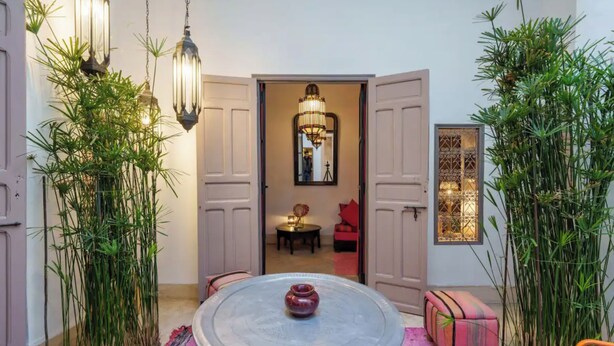 A round table with a vase, surrounded by chairs and a patterned rug. There are tall plants on either side and a hanging light fixture above. - Exclusive charming riad in the heart of the medina

10 mn from Jemaa el fna  (Marrakech)