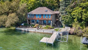 Ein zweigeschossiges Haus mit einem Steg, der in einen See führt, umgeben von dichten Bäumen.