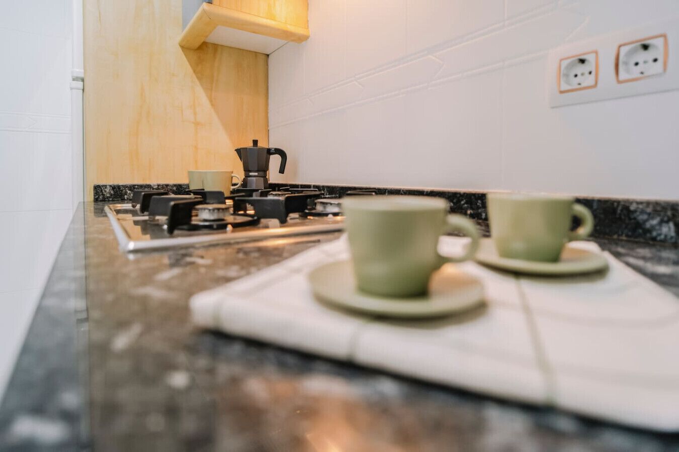 Une cuisine équipée d’une cuisinière à gaz, deux tasses vertes posées sur un plateau et une machine à café.