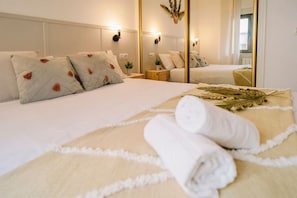 A neatly made bed with a white duvet, pillows with orange accents, and a rolled white towel on a beige bed runner. - 5min to Center| Wifi 1Gbps| Hospitals| University (Salamanca)