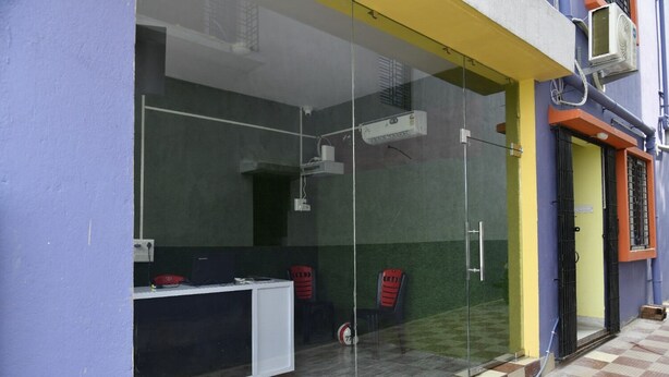A room with a glass partition, a desk, two chairs, and an air conditioning unit mounted on the wall. - MM Hotel and Service Apartment (Kolkata)