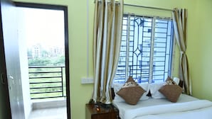 A hotel room with a bed, curtains, a window with bars, and a view of buildings and greenery outside. - MM Hotel and Service Apartment (Kolkata)