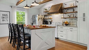 A kitchen with white cabinetry, a wooden ceiling, and a central island with chairs. - Kilted Cowboy - Cowboy Pool, Hot Tub & Fire Pit (Fredericksburg)