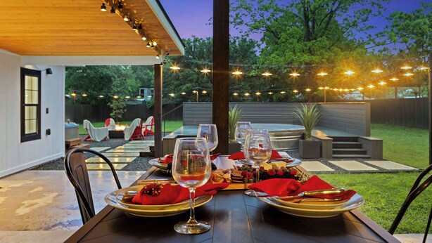 An outdoor dining area with a table set for two, surrounded by string lights and a view of the backyard. - Kilted Cowboy - Cowboy Pool, Hot Tub & Fire Pit (Fredericksburg)