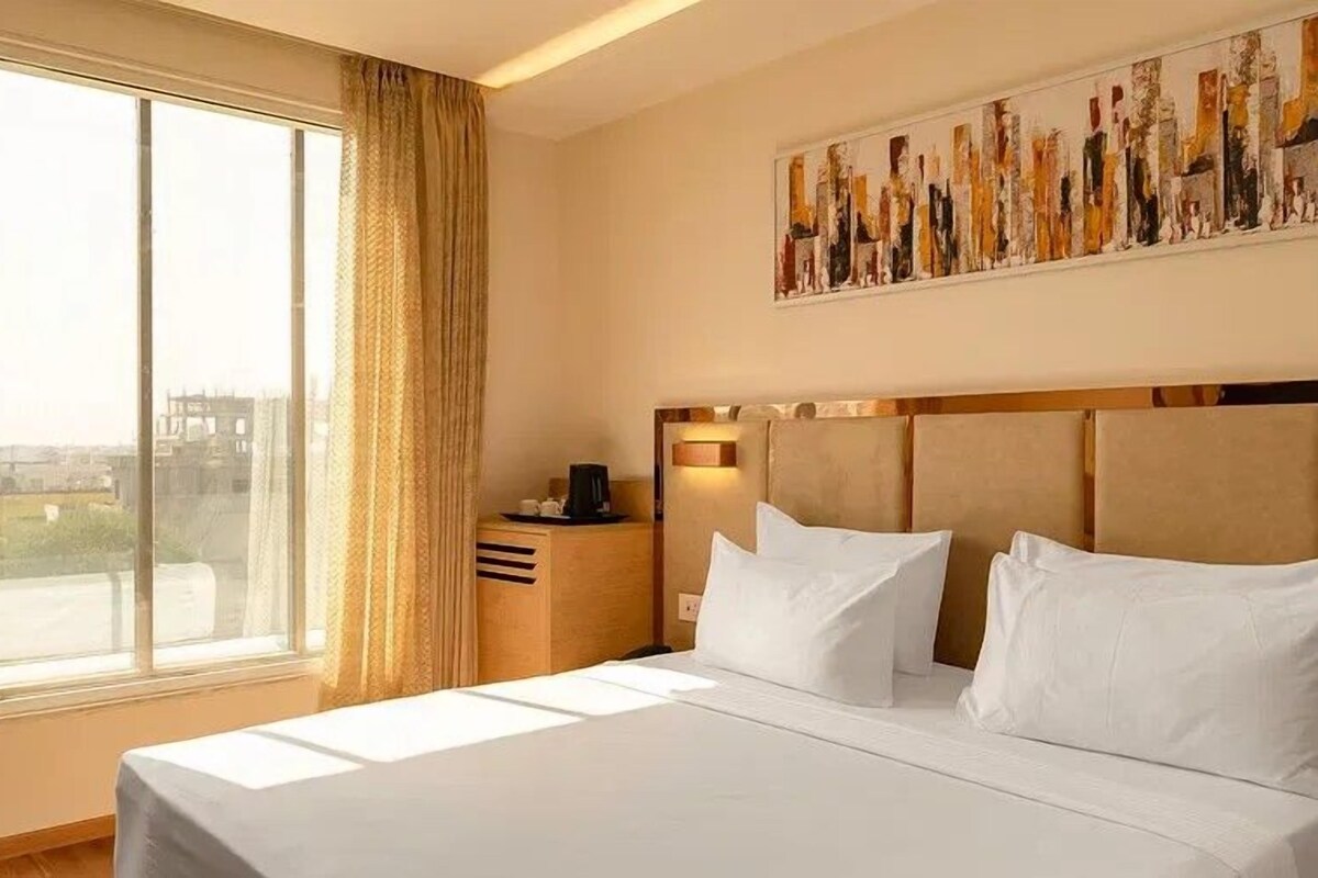 Una habitación de hotel con una cama grande, una mesita de noche, una cafetera y un cuadro en la pared.