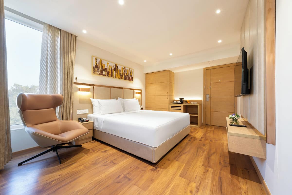 A modern hotel room with a large bed, a sitting area, a desk, and a TV mounted on the wall.