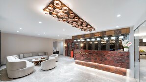 Moderne reception med en marmor-receptionistskranke, siddeområde med sofaer og lænestole, samt et unikt loftslampe.