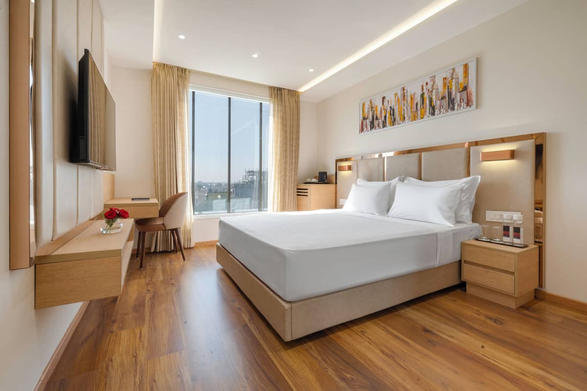 A modern hotel room with a large bed, a desk, a chair, a TV, and a window with a view.