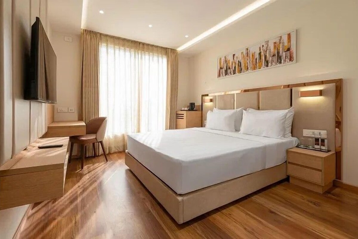 Una habitación de hotel con una cama grande, un escritorio, una silla, un televisor y un cuadro en la pared.