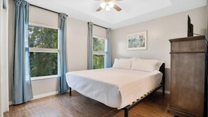 A bedroom with a bed, two windows with curtains, a ceiling fan, a painting on the wall, and a wooden cabinet. - Family escape near Disney parks w/ resort access (Kissimmee)