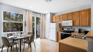 A modern kitchen with wooden cabinets, a white refrigerator, a stove, and a dining area with a table and chairs. - Family escape near Disney parks w/ resort access (Kissimmee)