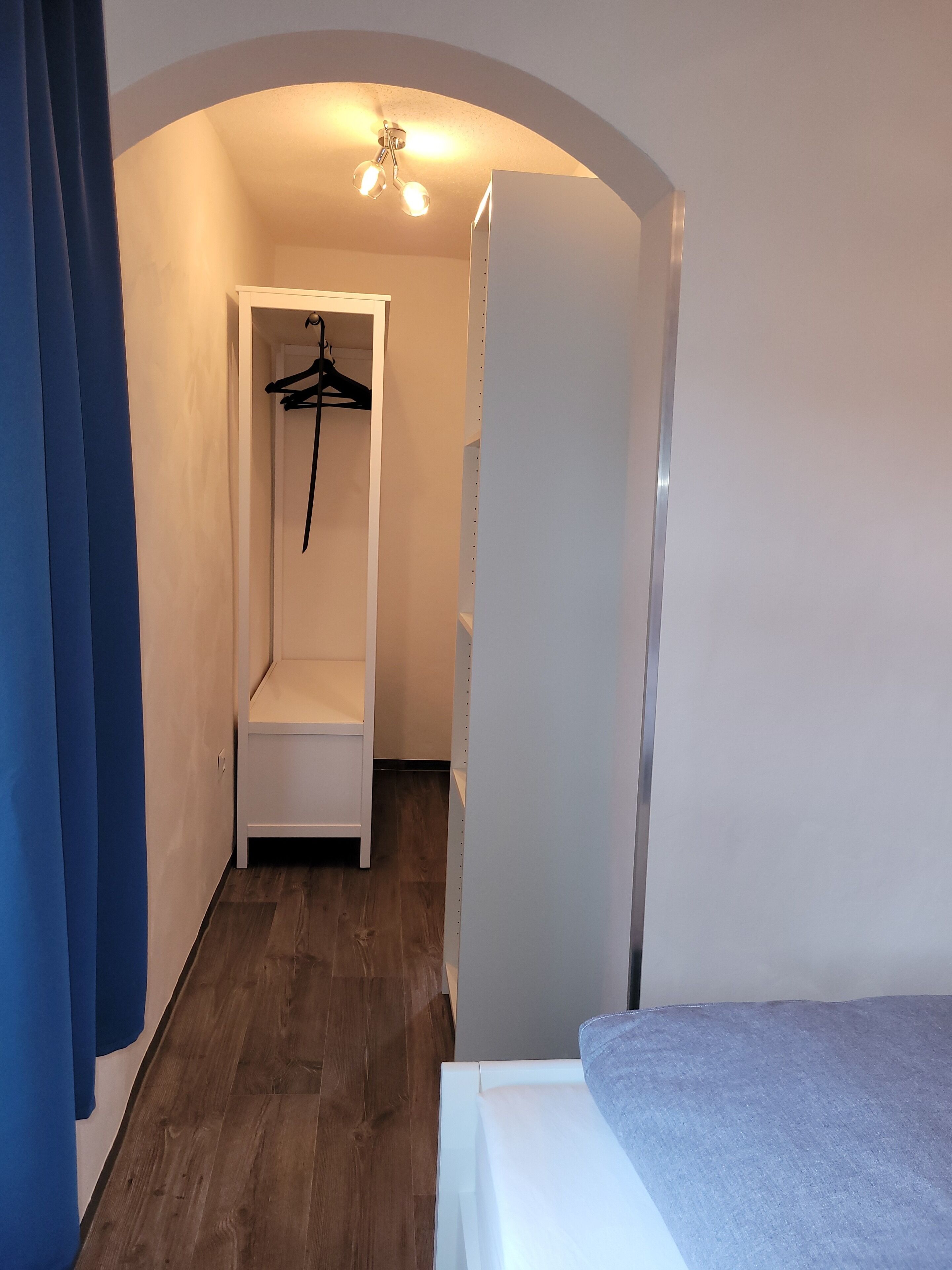 A narrow hallway with a bench, a coat rack, and a bed.