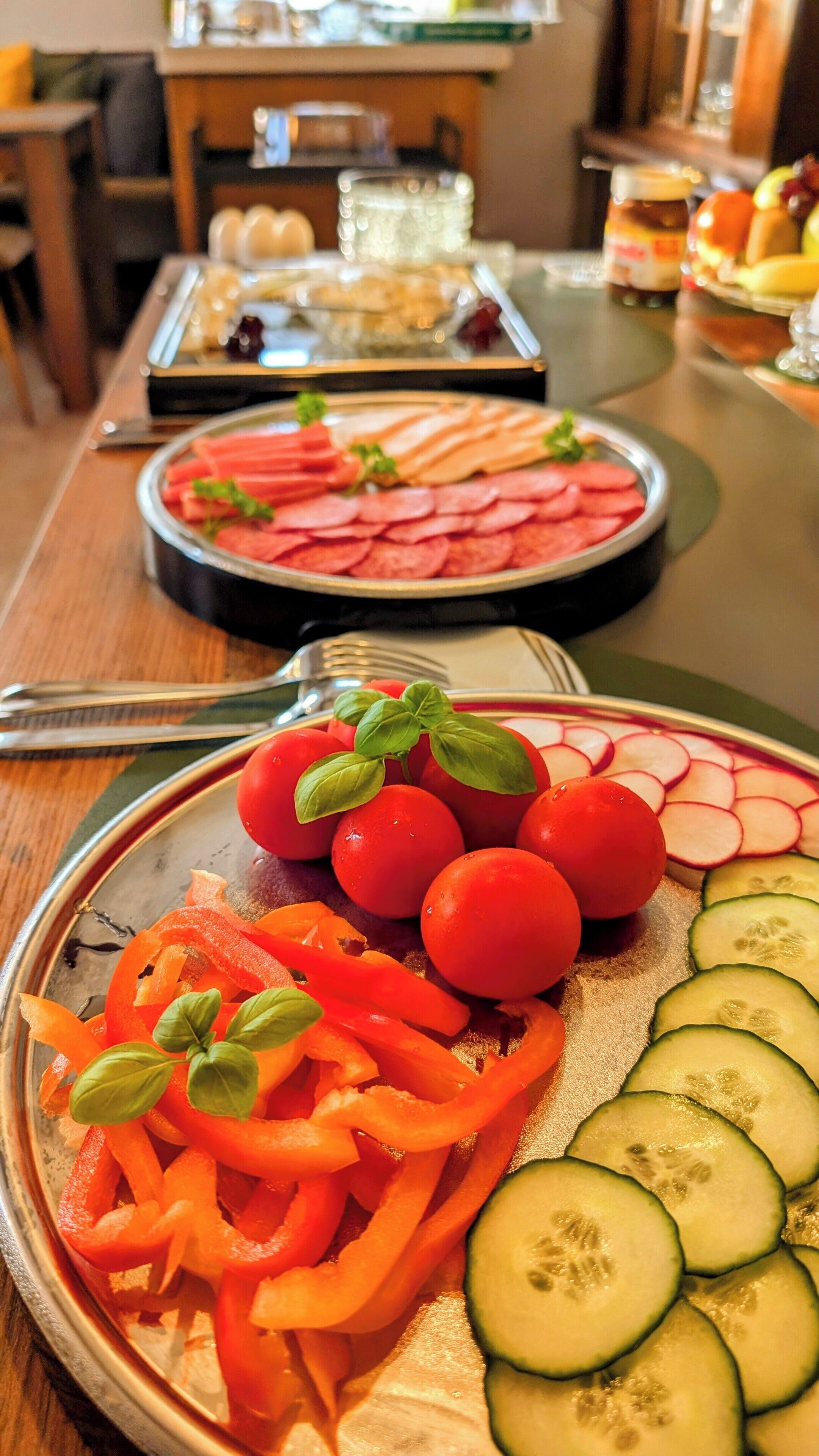 Una mesa de buffet con diversos alimentos, incluyendo pepinos en rodajas, tomates cherry y palitos de zanahoria.