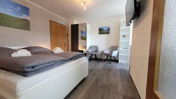 Ein Schlafzimmer mit einem Bett, zwei Stühlen, einem Fernseher und einem Regal.